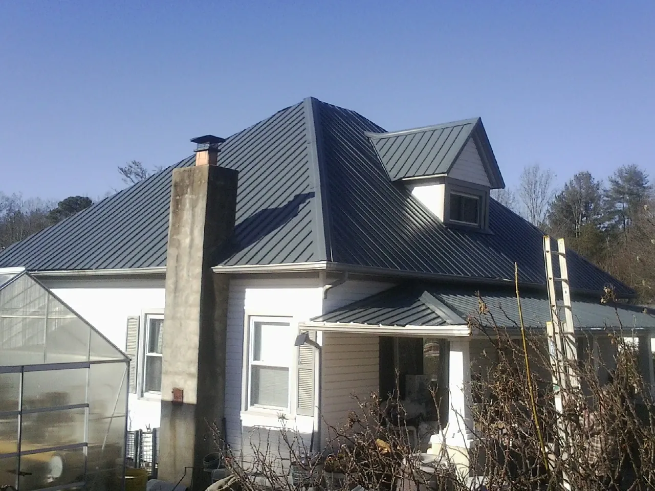 Dark blue standing seam metal roof on a white farmhouse with dormer — Slate & Tile Roof Repair by Roofing Brothers in Lake Wilson
