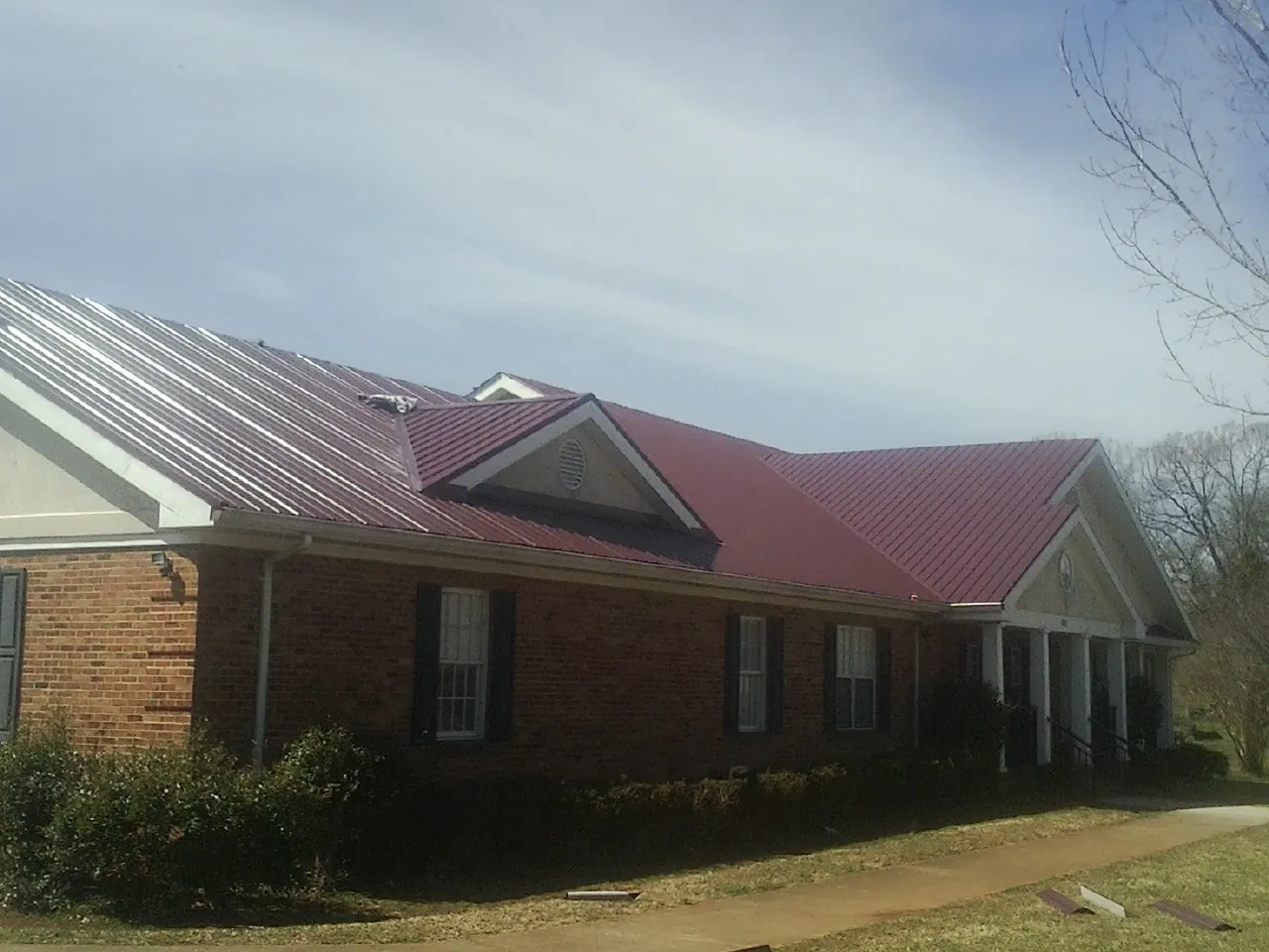 Red metal roof with gabled entries on a long brick building, from a Hail Damage Roof Repair job in Lake Wilson