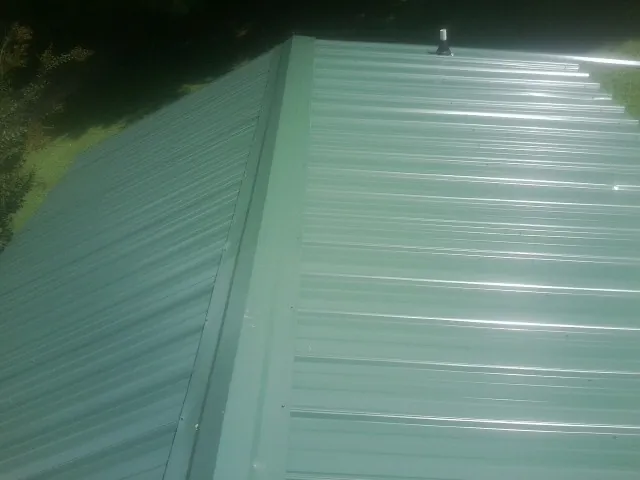 New green metal panels meeting at the ridge of a roof — Flat Roof Repair work by our crew in Lake Wilson