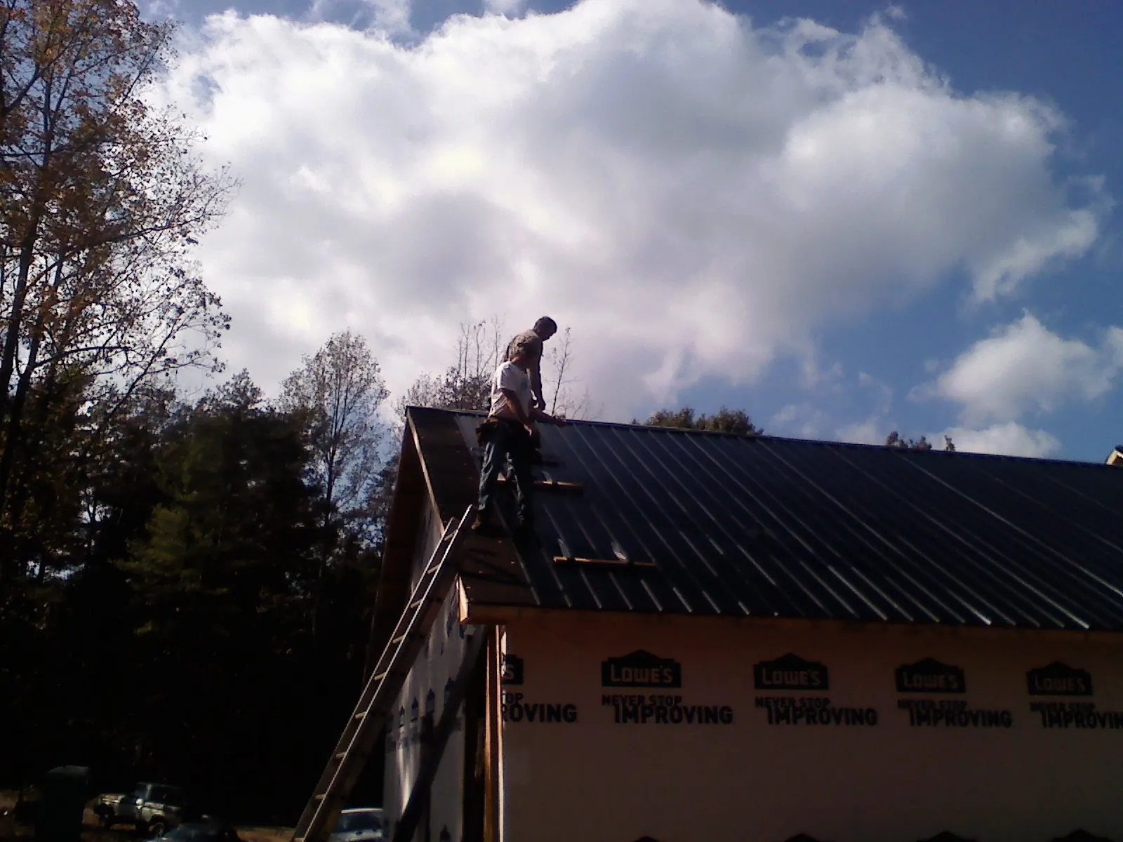 Roofer fastening dark metal panels high against a cloudy sky, from a Roof Inspection job in Lake Wilson
