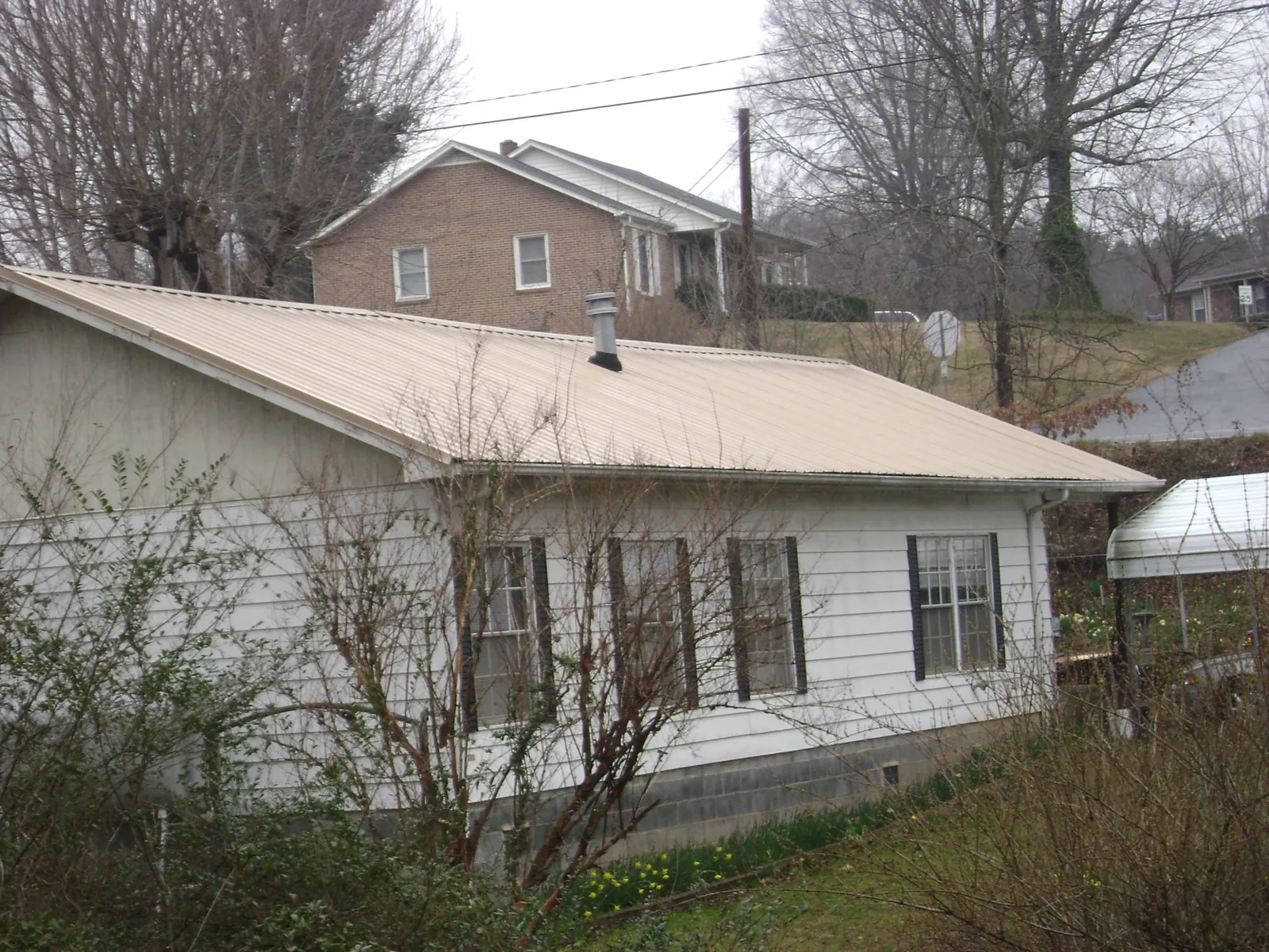 Tan metal roof on a white sided house set into a hillside — Commercial Roofing by Roofing Brothers in Lake Wilson