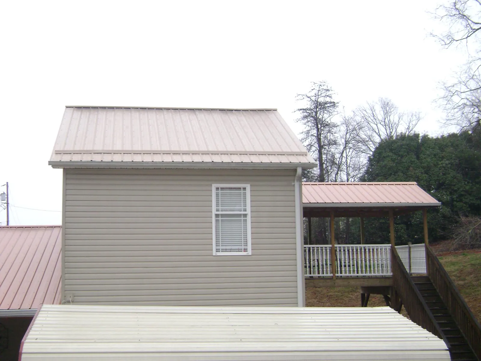 Tan metal roofs on a two story addition and attached porch, from a Roof Replacement job in Lake Wilson